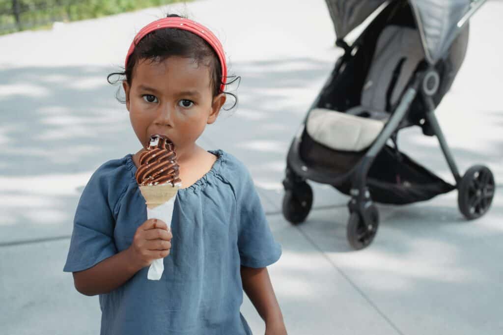 A kid is eating an ice cream in a park on a hot summer day